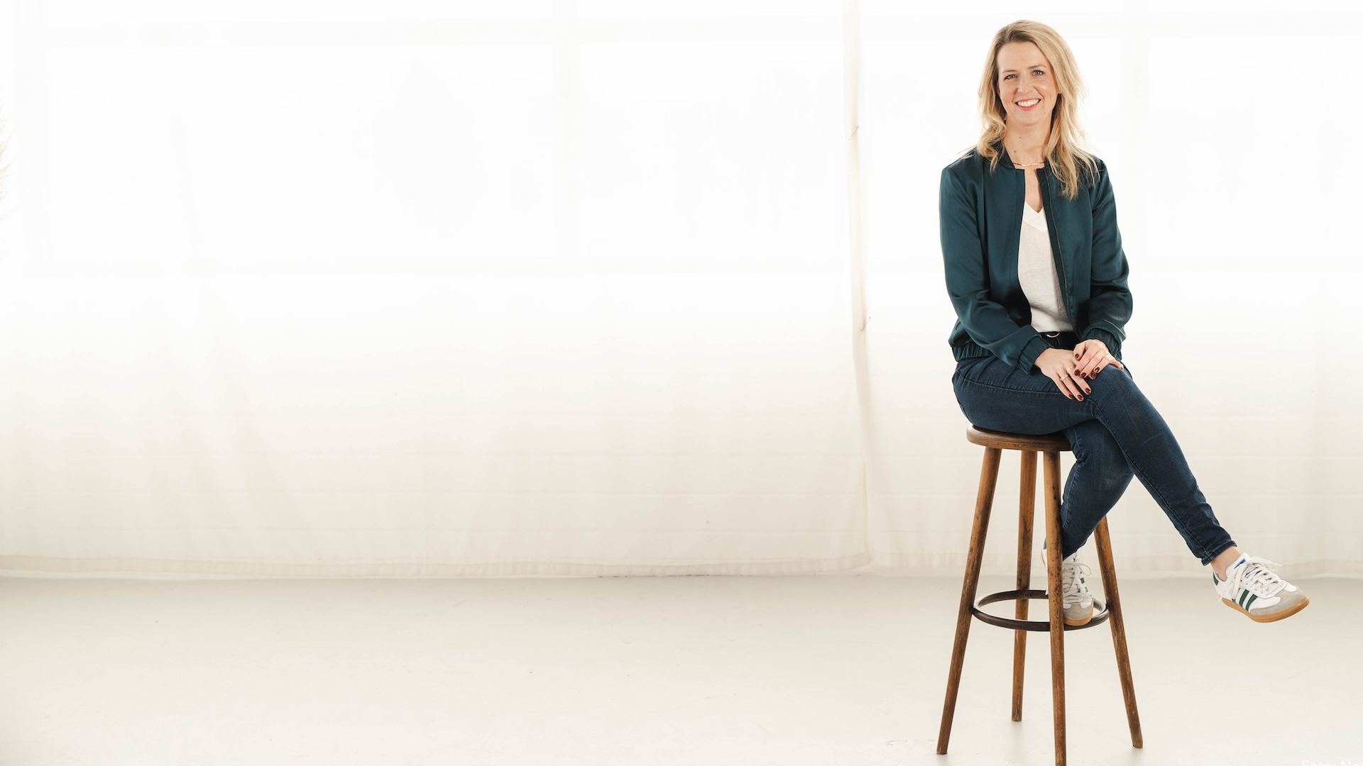 Iris Schulz sitzt auf einem Barhocker und schaut freundlich lächelnd in die Kamera