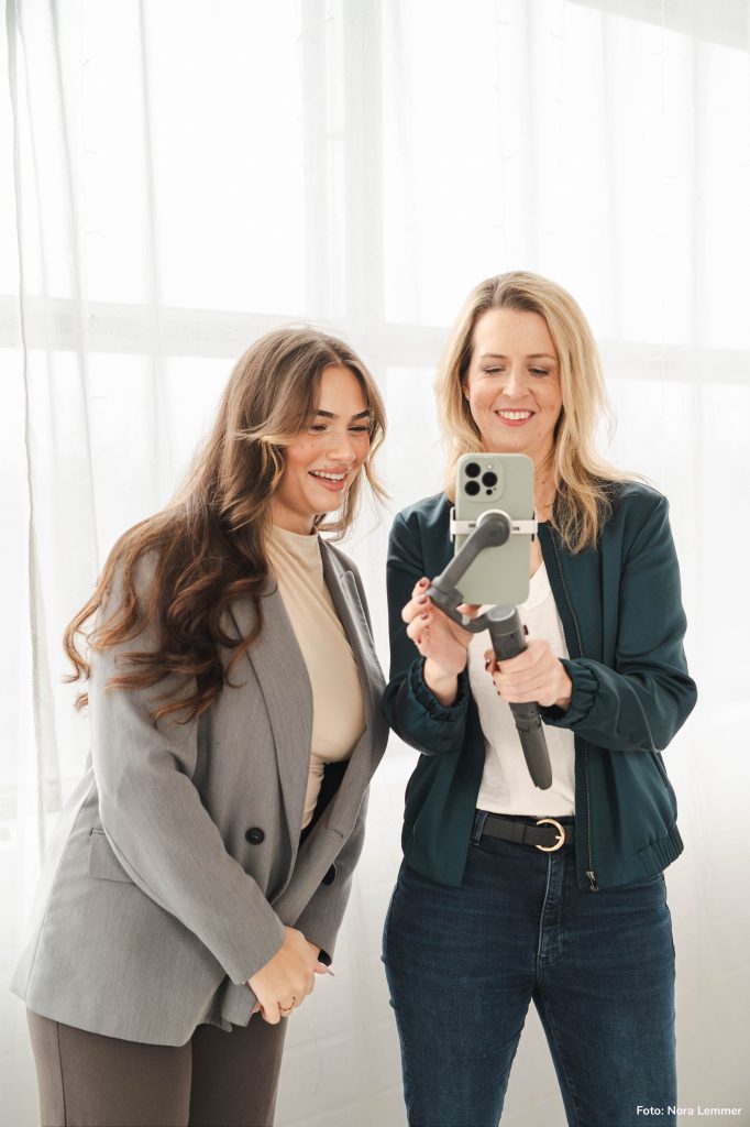 Iris Schulz schaut mit einer Kundin gemeinsam auf ein Handy, das in ein Gimbal eingespannt ist